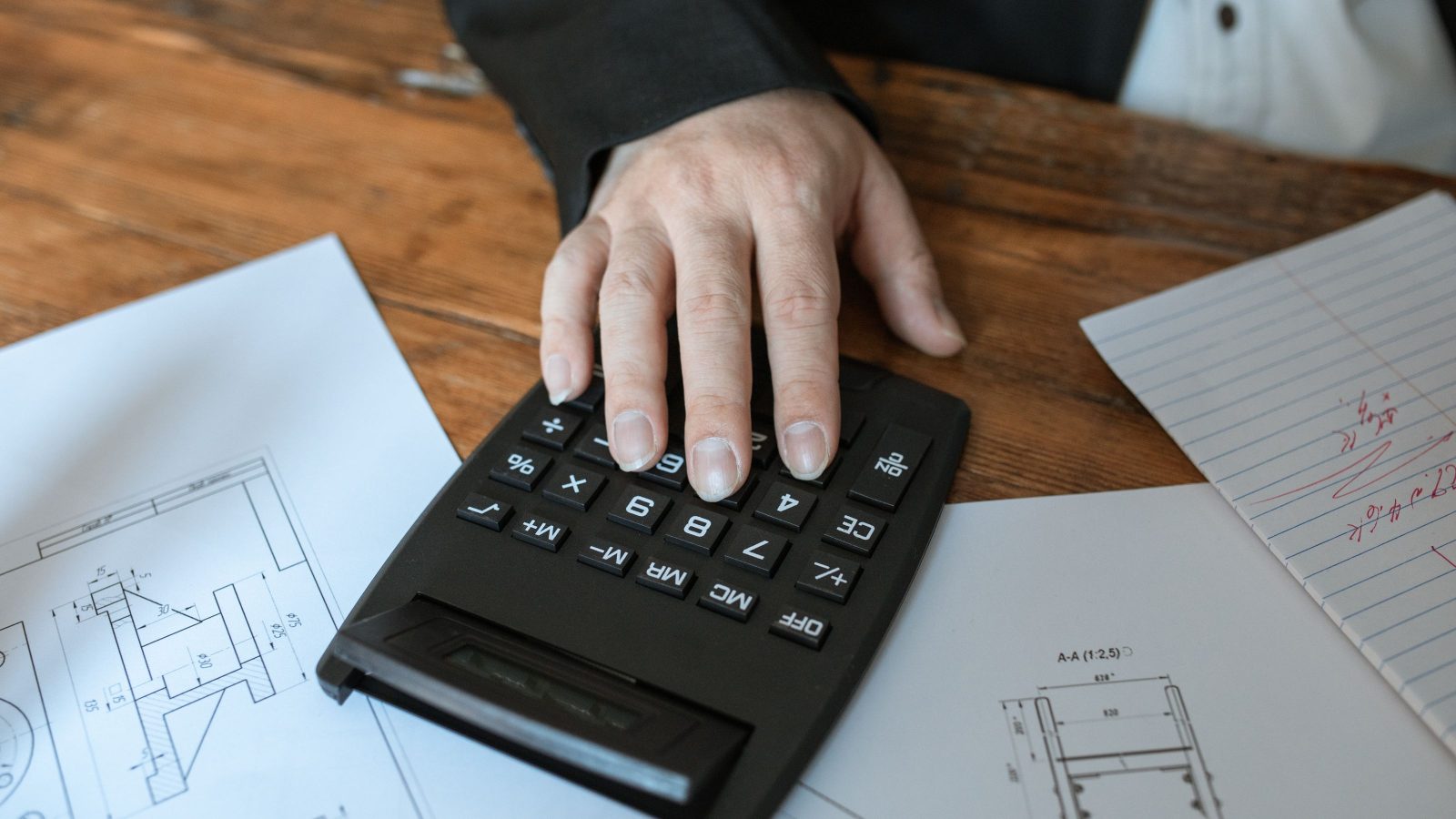 Hands working through figures on a calculator beside printed documents.